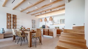 Una cocina moderna con vigas de madera, una zona de comedor con sillas de mimbre y una escalera.