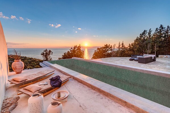 A rooftop pool with lounge chairs and a view of the sunset over the ocean.