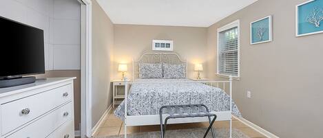 A bedroom with a bed, bedside tables, a TV, and a chair.