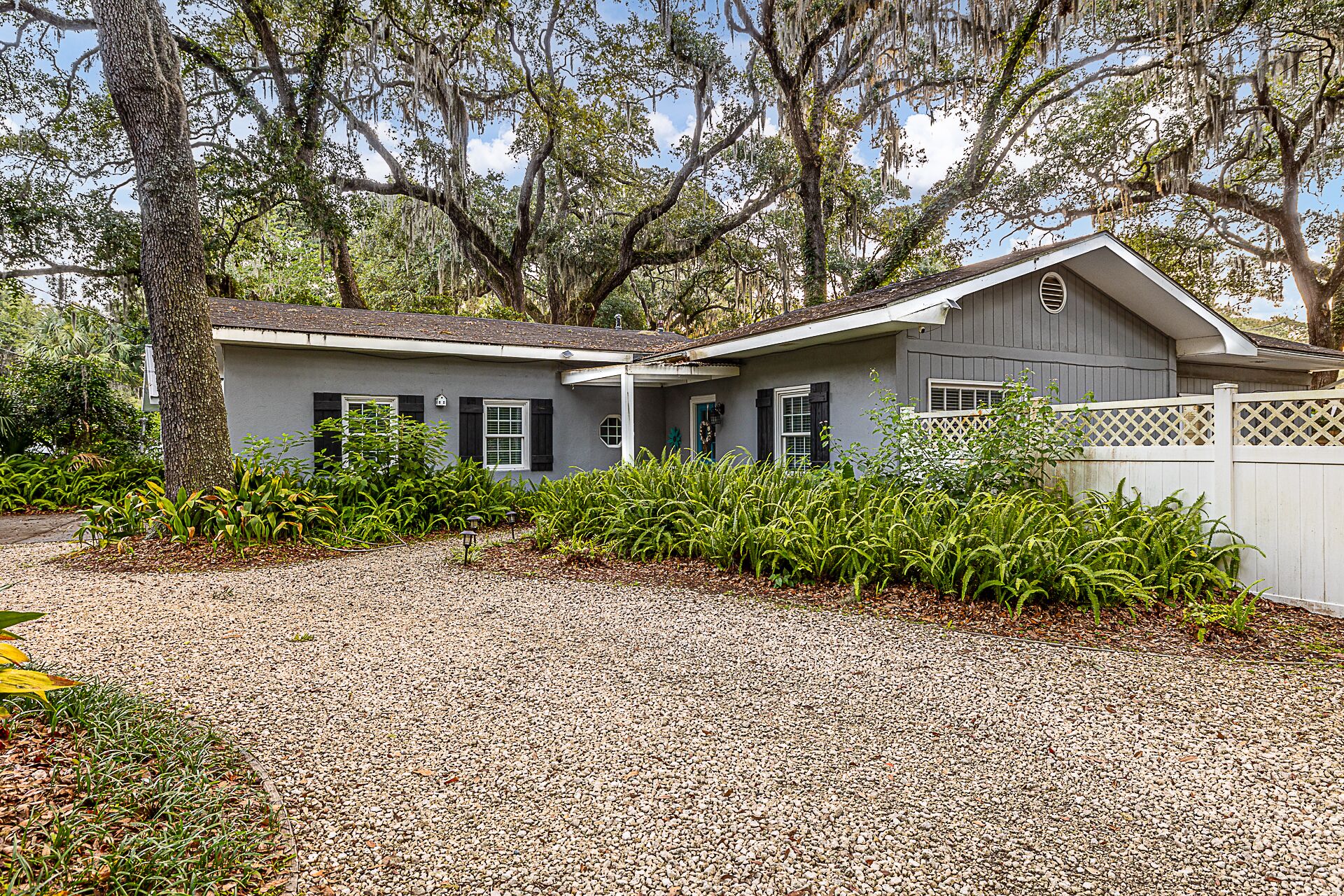 A two-story house with a gray exterior, a front porch, and a gravel driveway.