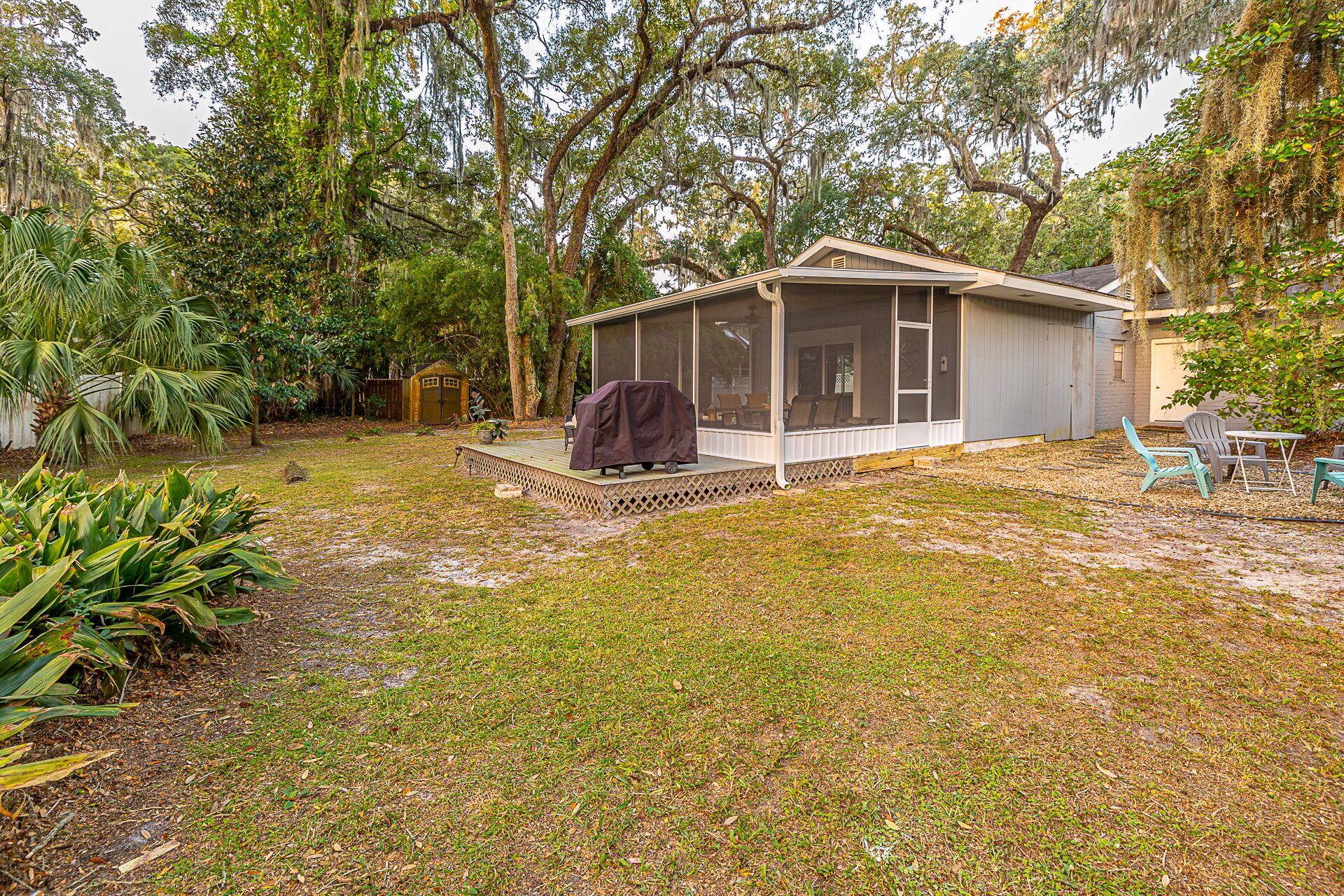 A house with a covered porch, a small shed, and a lawn with tropical plants.