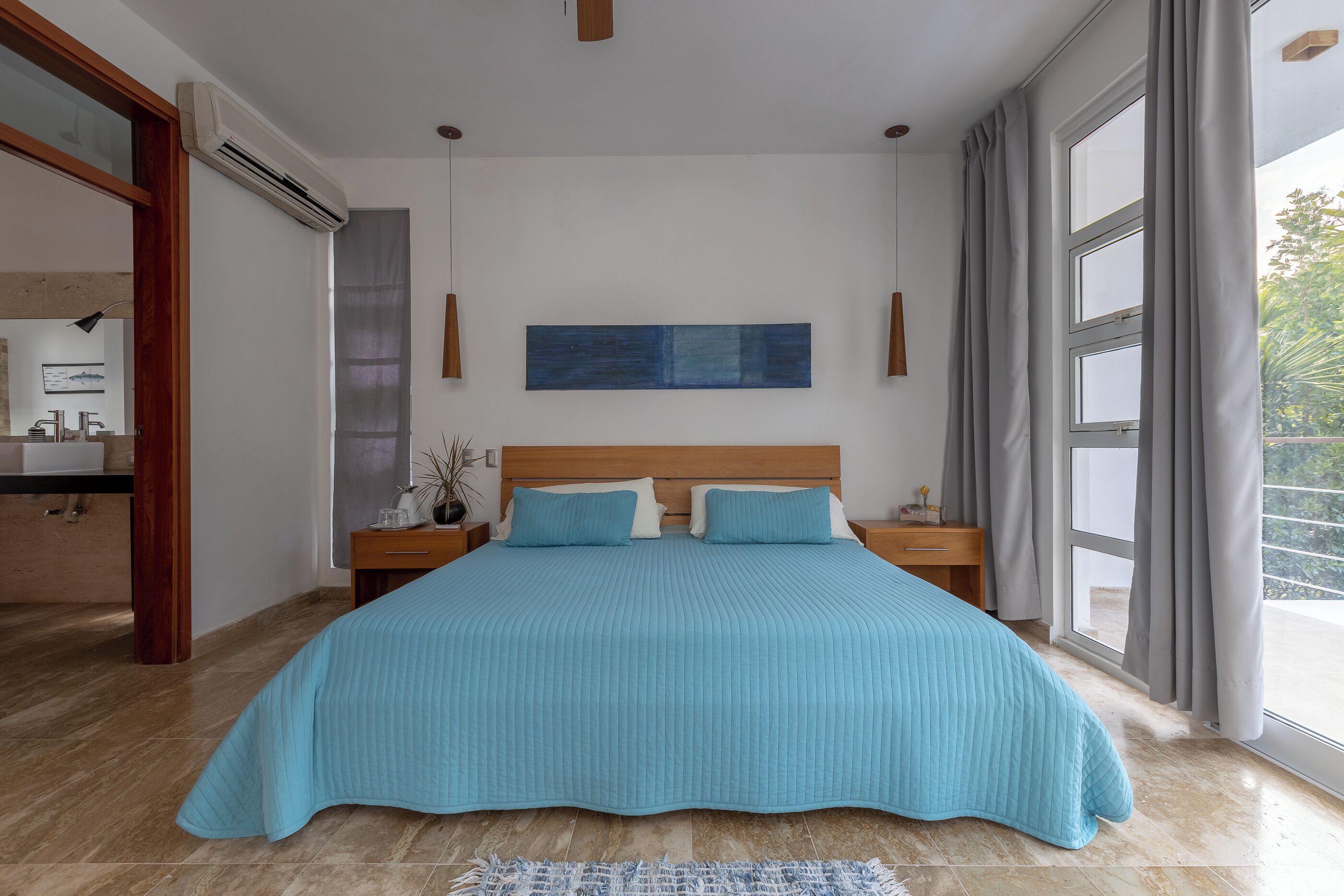 A bedroom with a large bed, a nightstand, a bedside table, a window with curtains, and a wall-mounted artwork.