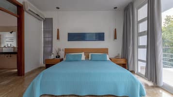 A bedroom with a large bed, a nightstand, a bedside table, a window with curtains, and a wall-mounted artwork.