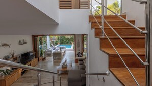 Ein modernes Interieur mit einer Treppe, Holzboden, einem Flachbildfernseher und einem Pool, der durch eine offene Tür sichtbar ist.