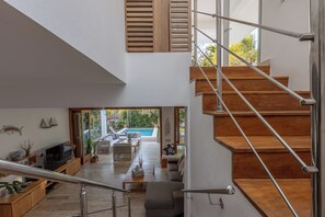 Un intérieur moderne avec un escalier, un plancher en bois, un téléviseur à écran plat et une piscine visible à travers une porte ouverte.