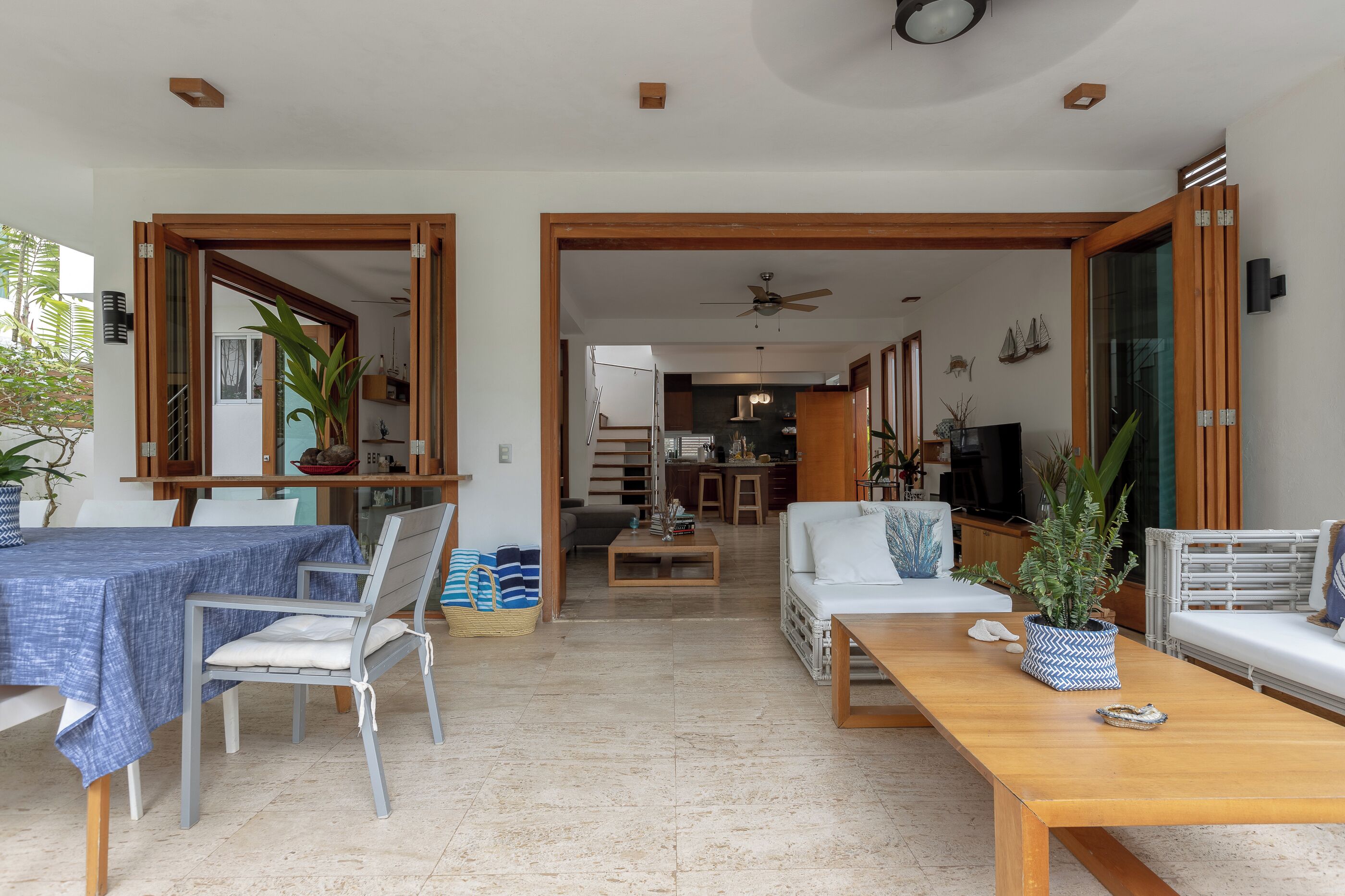 Amplia sala de estar con una mesa de comedor, sillas, un sofá y una mesa de centro. Se observa una cocina al fondo, un ventilador de techo y un televisor sobre un mueble.