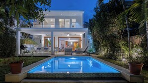 Ein modernes, zweistöckiges Haus mit Swimmingpool, Sitzgelegenheiten im Freien und Grillplatz.