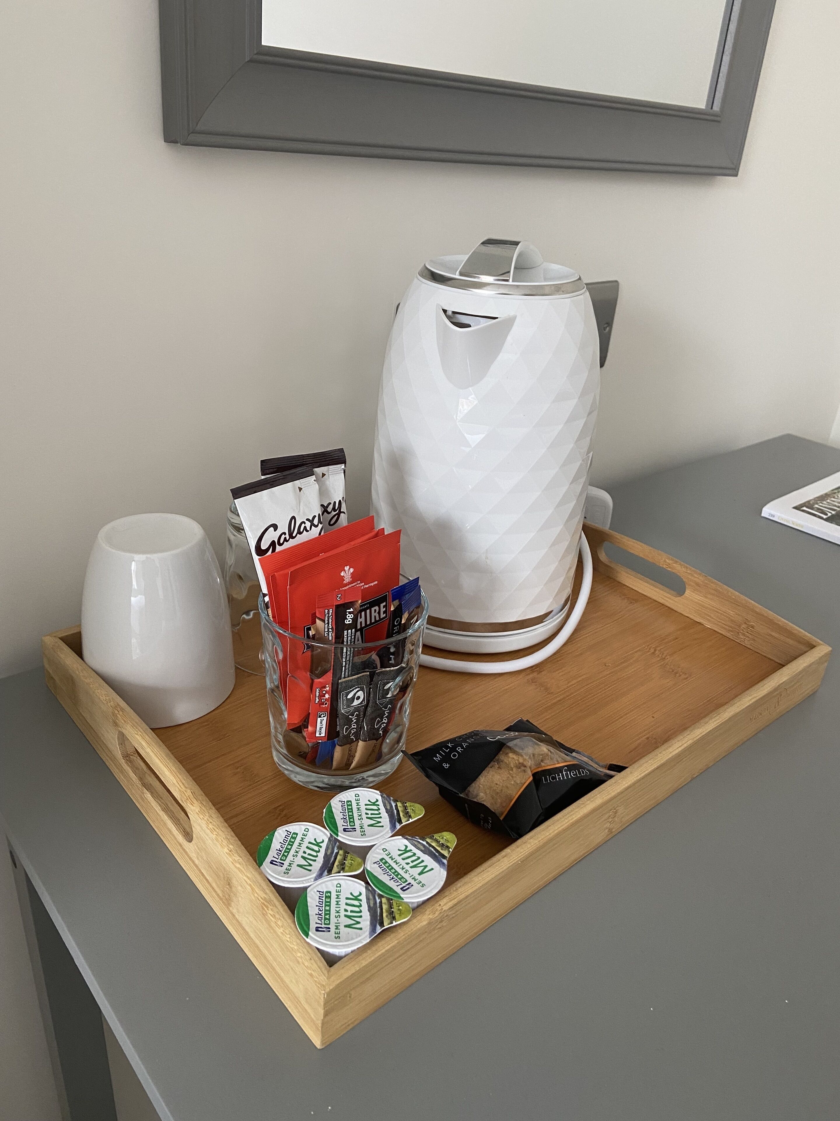 A tray with a coffee maker, a glass jar of chocolates, a mug, and a box of milk.