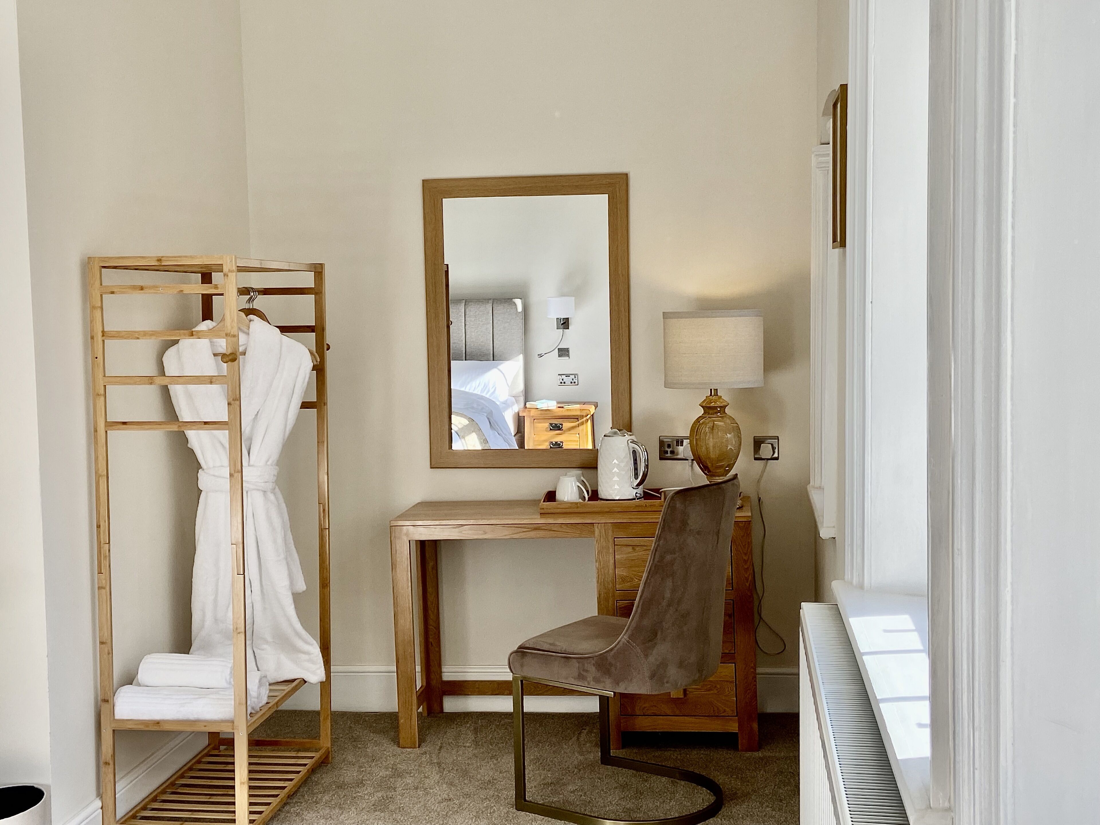 A hotel room with a wooden desk, a chair, a mirror, a radiator, and a radiator cover.