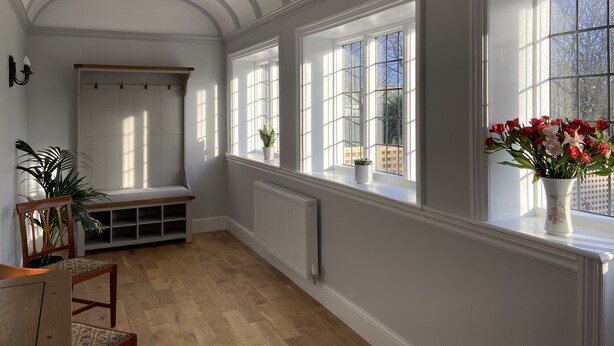 A room with a high ceiling, large windows, a bench, a radiator, and a potted plant. - Red Barns Bed & Breakfast (Redcar)