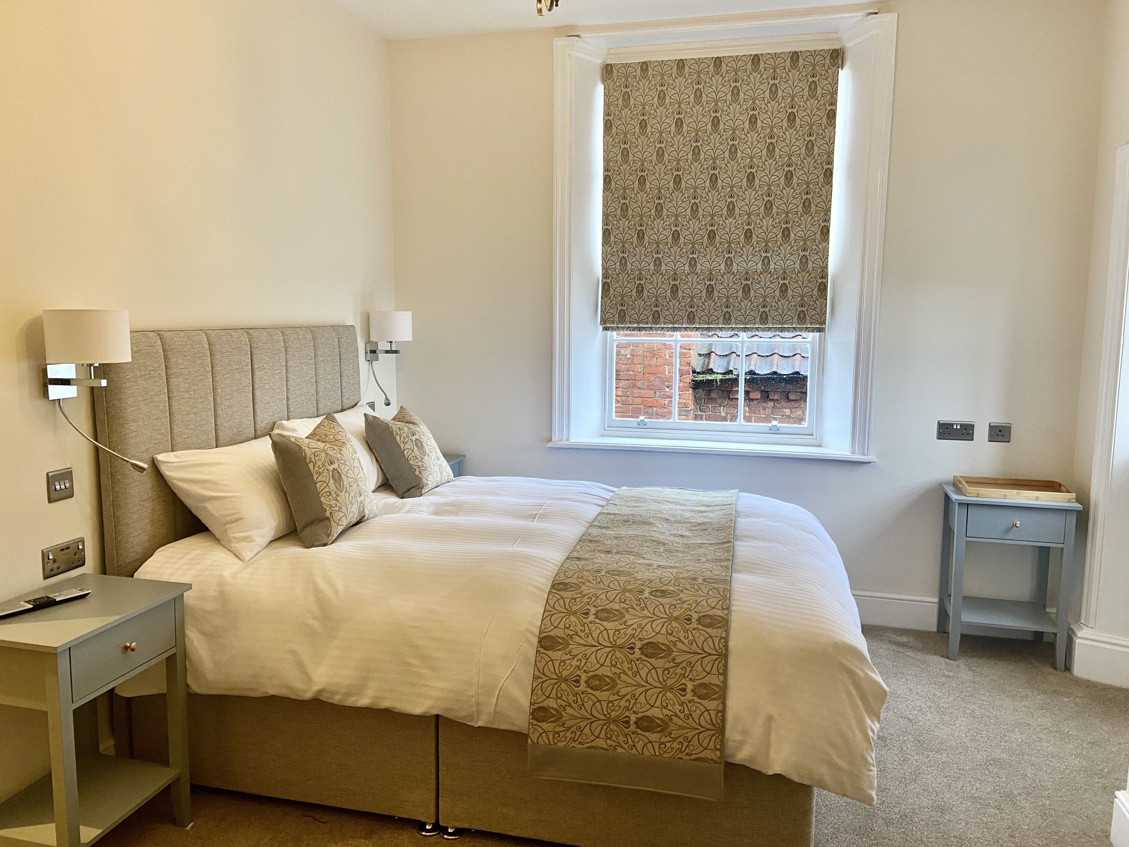 A neatly arranged bedroom with a large bed, bedside tables, a window with a view, and a small nightstand.