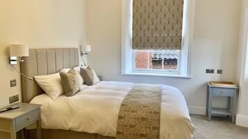 A neatly arranged bedroom with a large bed, bedside tables, a window with a view, and a small nightstand.