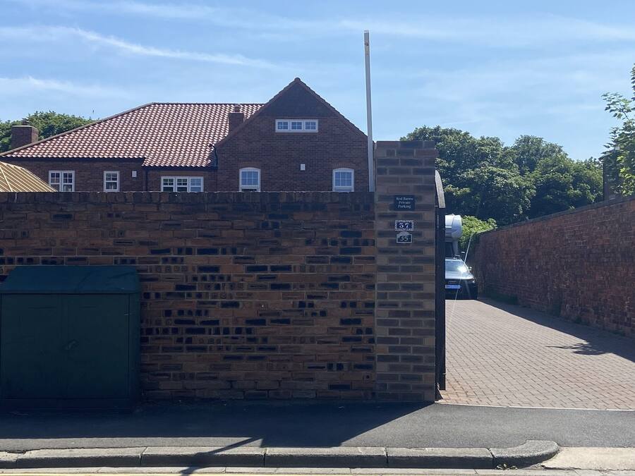 A brick building with a tiled roof, a green gate, and a sign indicating 'Red Barn Private Parking'.