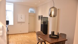 Spiseområde med et træbord, fire stole, en hængende lampe og billedkunst på væggene.