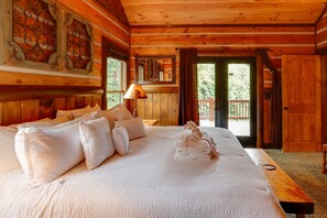 A wooden cabin bedroom with a large bed, a bench, and a balcony door.
