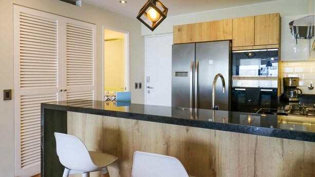 A modern kitchen with wooden cabinets, a stainless steel refrigerator, and a black countertop. - w* | Remarkable 1BR with Balcony in Miraflores (Miraflores)