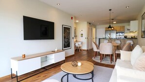 A modern living room with a white sofa, a round coffee table, and a TV mounted on the wall. There is a dining area with a table and chairs in the background. - w* | Remarkable 1BR with Balcony in Miraflores (Miraflores)