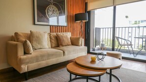A modern living room with a sofa, a round coffee table, a clock on the wall, and a balcony with outdoor furniture. - w* | Remarkable 1BR with Balcony in Miraflores (Miraflores)