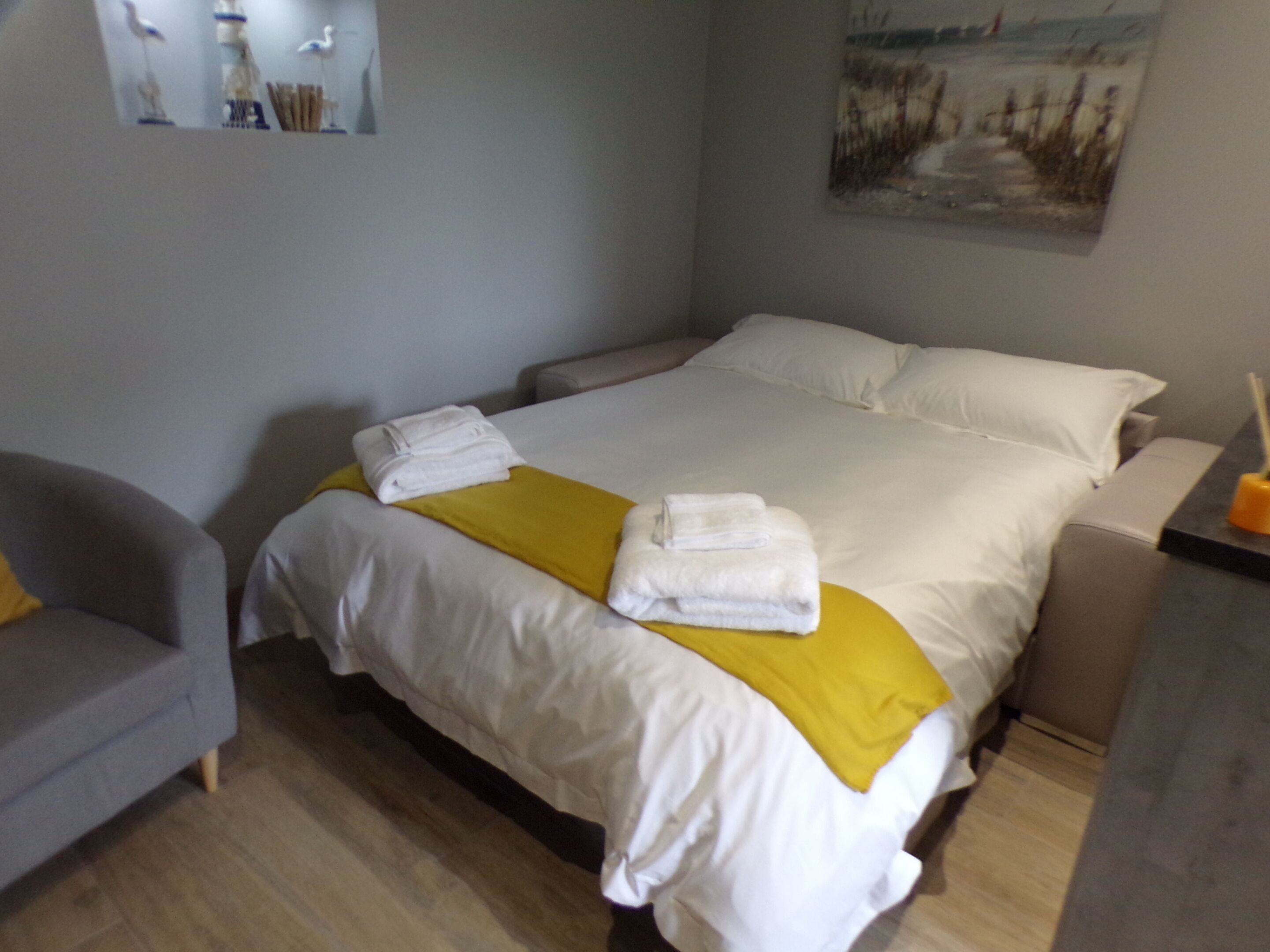 A hotel room with a bed, a chair, and a painting on the wall.