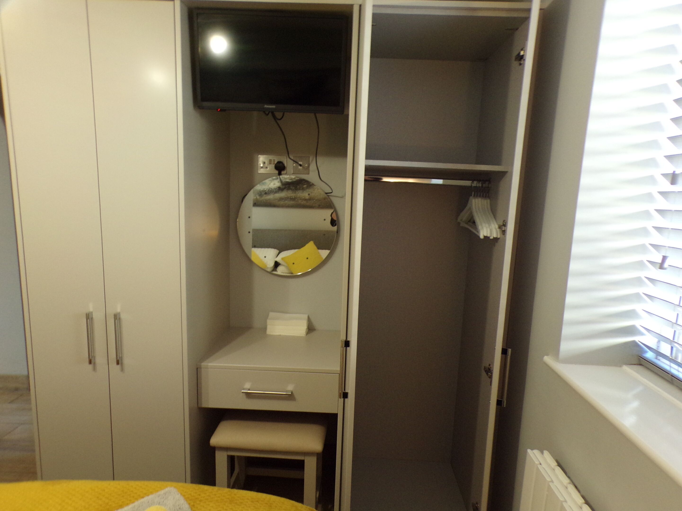 A bedroom with a bed, a wardrobe, a mirror, and a television.