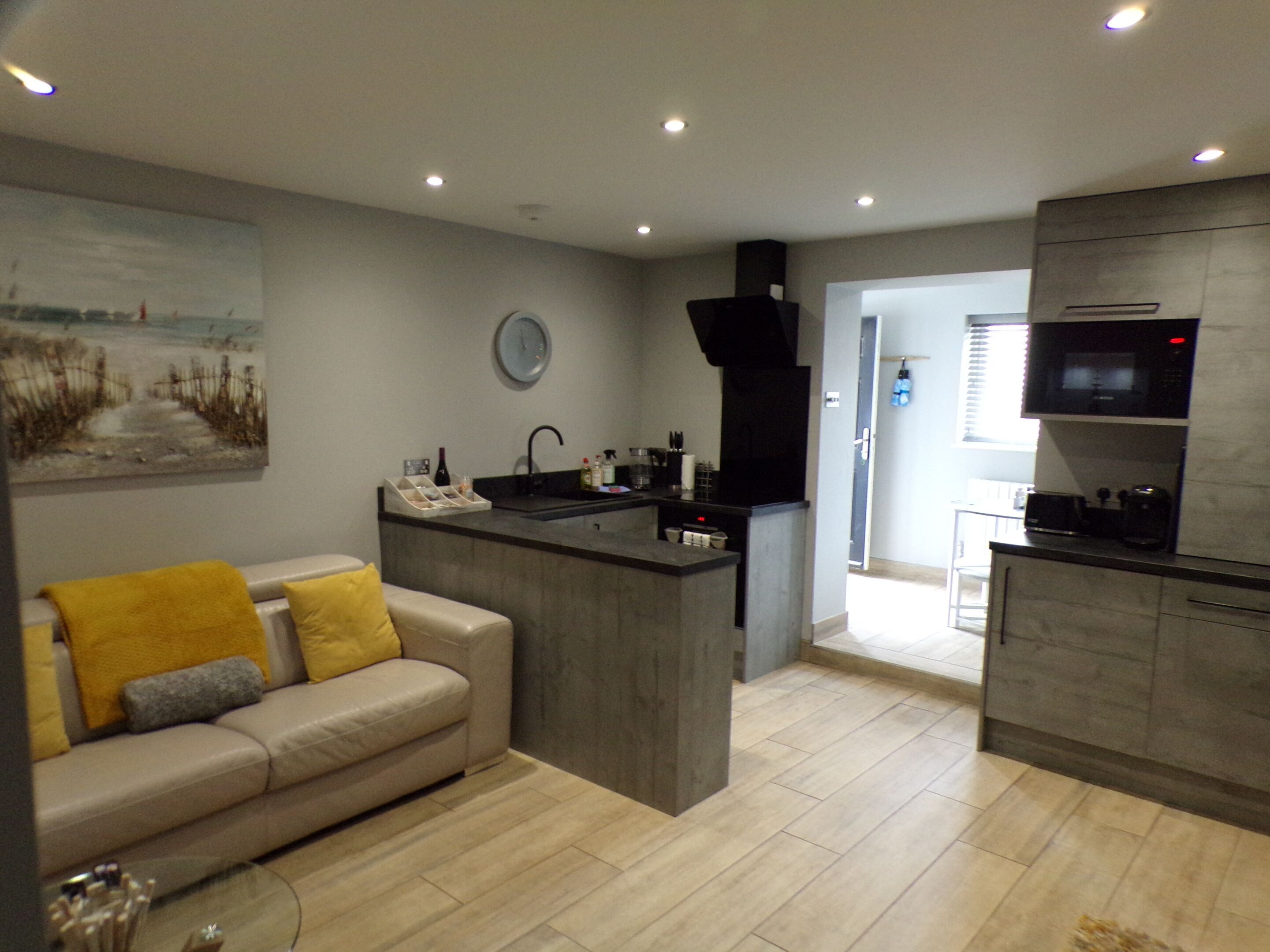 A modern kitchen with a central island, a dining area with a sofa, and a living room with a painting on the wall.