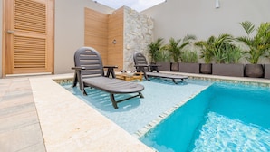 Zona de piscina con sillas de descanso, pared de piedra y plantas en macetas.