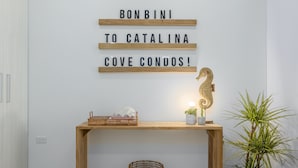 Un interior moderno con una consola de madera, un letrero decorativo, una cesta tejida y una planta en maceta.