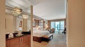 Ein modernes Hotelzimmer mit einem großen Bett, einer Sitzecke mit Stuhl und Tisch, einem großen Spiegel und Blick auf die Stadt durch das Fenster.
