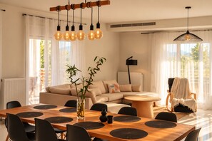 A modern living room with a sofa, dining table, and chairs. There is a plant on the table and a lamp in the corner.