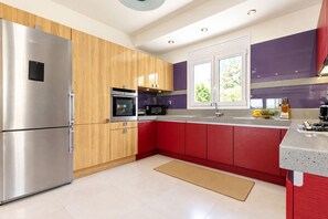 Eine moderne Küche mit Edelstahlkühlschrank, Holzschränken, einer roten Kücheninsel und einem Fenster, das für natürliches Licht sorgt.