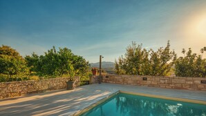 A swimming pool with a stone wall and potted plants, surrounded by trees and a view of distant mountains. - Blue Sky Villa in Crete (Επάνω Βαθειά)