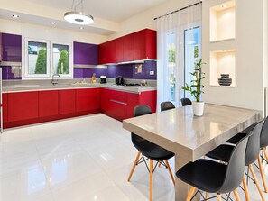 A modern kitchen with red and purple cabinets, a large island with chairs, and a view of greenery outside.