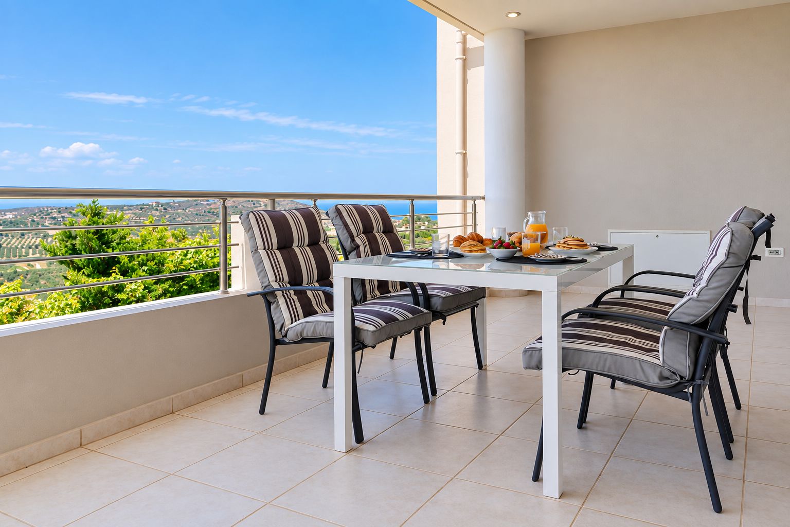 Un balcon avec une table et des chaises, une vue sur la verdure et un paysage lointain, et une table préparée pour le petit-déjeuner.