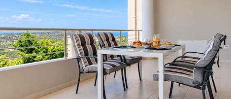 A balcony with a table and chairs, a view of greenery and a distant landscape, and a breakfast setup.