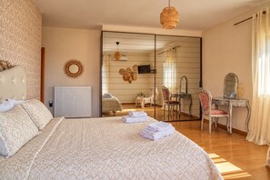 A hotel room with a large bed, a sitting area with a chair and table, a vanity with a mirror, and a view through a sliding door.