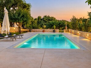 A rectangular swimming pool with a stone wall and potted plants around it.
