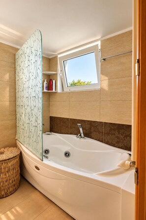 A modern bathroom with a freestanding bathtub, a window with a view, and a decorative bamboo-patterned panel.