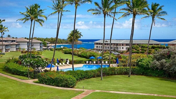 A resort with a pool, palm trees, and ocean views. - Poipu Sands 124 Steps to Shipwreck Beach By Suite Paradise (Koloa)