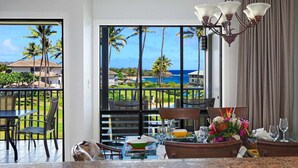 A hotel room with a balcony, a dining area, and a view of palm trees and the ocean. - Poipu Sands 124 Steps to Shipwreck Beach By Suite Paradise (Koloa)