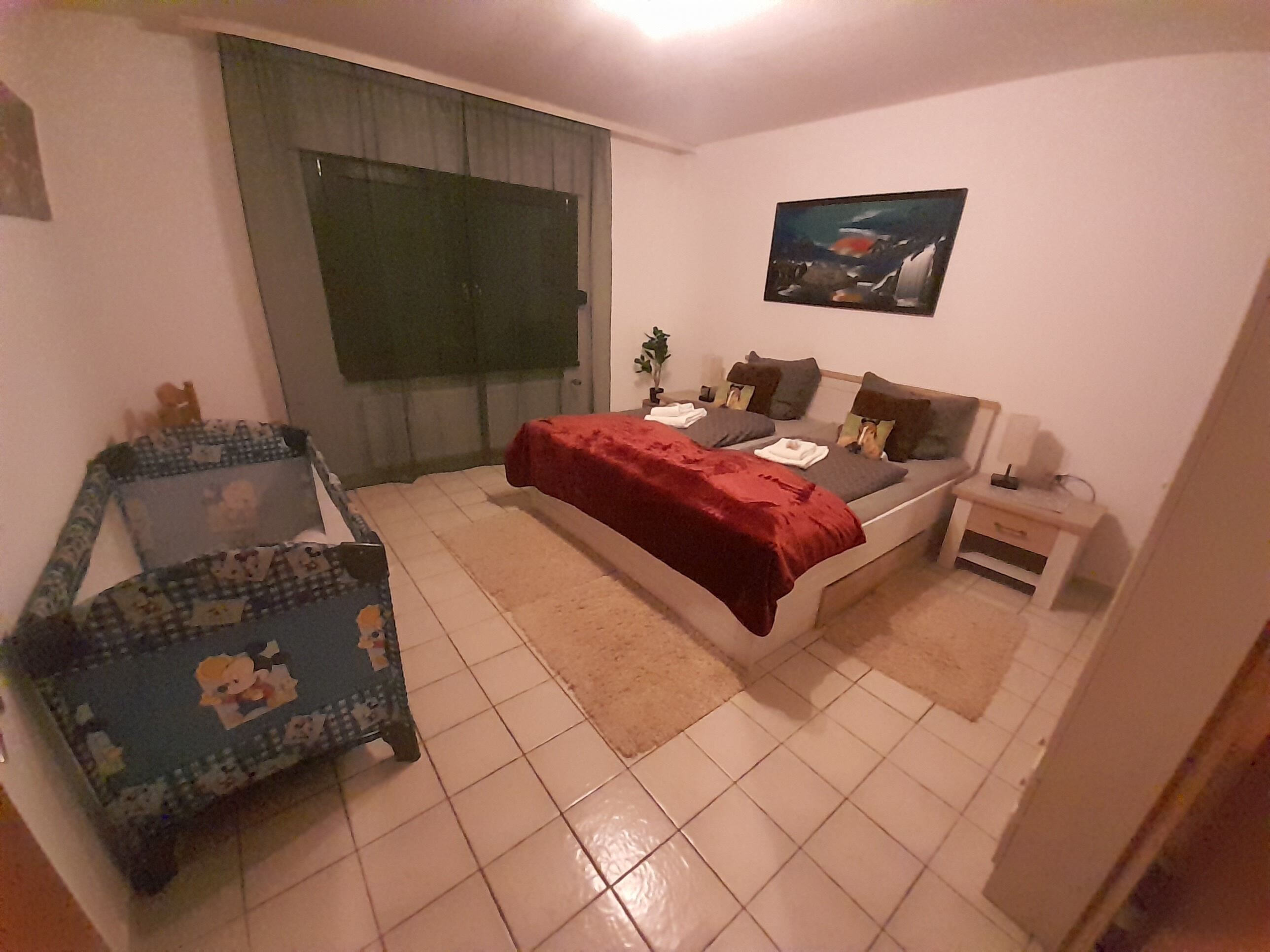 Et soveværelse med seng, stol, lille bord, et vindue og et billede på væggen.