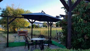 Een overdekt terras met een tafel, stoelen, een barbecue en uitzicht op een veld.
