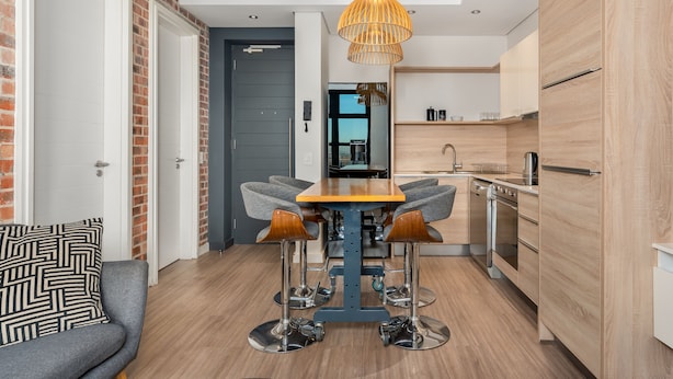 A modern kitchen with a wooden table, bar stools, and a hanging light fixture. - Matrix 504 (Cape Town)