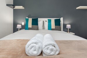 A neatly made bed with white towels, a grey headboard, and teal and grey pillows. - Matrix 504 (Cape Town)
