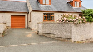 Ein zweistöckiges Haus mit Garage, Blumenbeet mit rosa Blüten und geneigtem Dach.