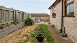 Ein Garten mit Holzzaun, Beton Terrasse und einem Haus mit Fenster.