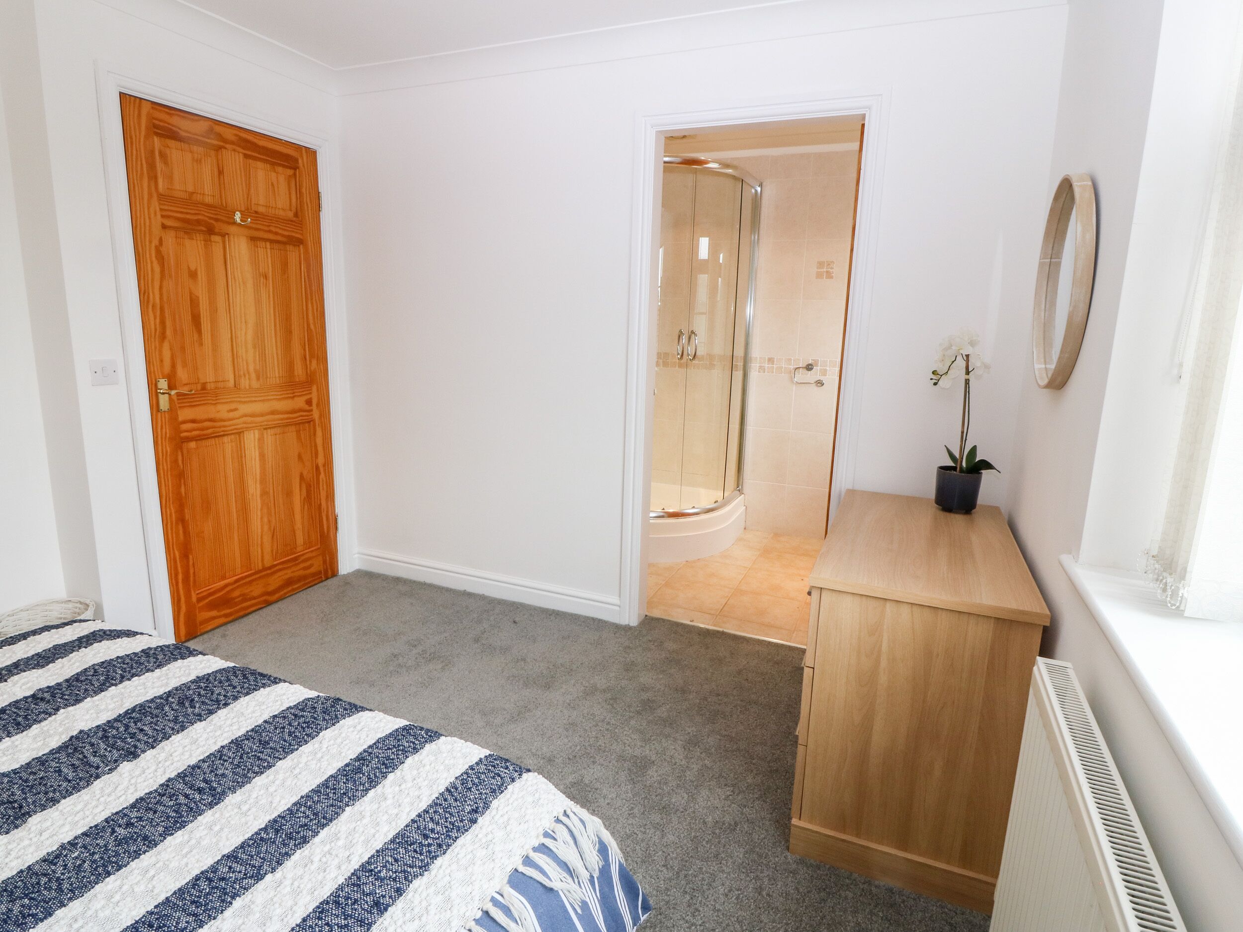 Un dormitorio con puerta de madera, ducha, tocador de madera y cama con ropa de cama a rayas.