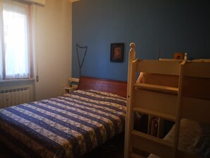 Un dormitorio con literas, una mesita de noche, una ventana con cortinas y un cuadro colgado en la pared.