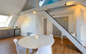 Une cuisine moderne avec une table de salle à manger ronde, des chaises blanches et une lucarne.