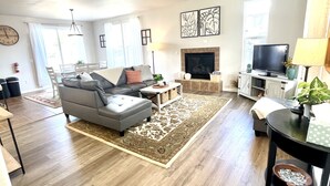 A spacious living room with a grey sofa, a fireplace, a television, and a dining area with a table and chairs. - Close to Montgomery Village and Flamingo Resort, just minutes to wineries (Santa Rosa)