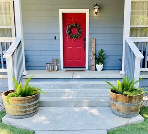 A red door with a wreath, two wooden lanterns, a welcome sign, and two wooden planters with greenery on a porch. - Close to Montgomery Village and Flamingo Resort, just minutes to wineries (Santa Rosa)